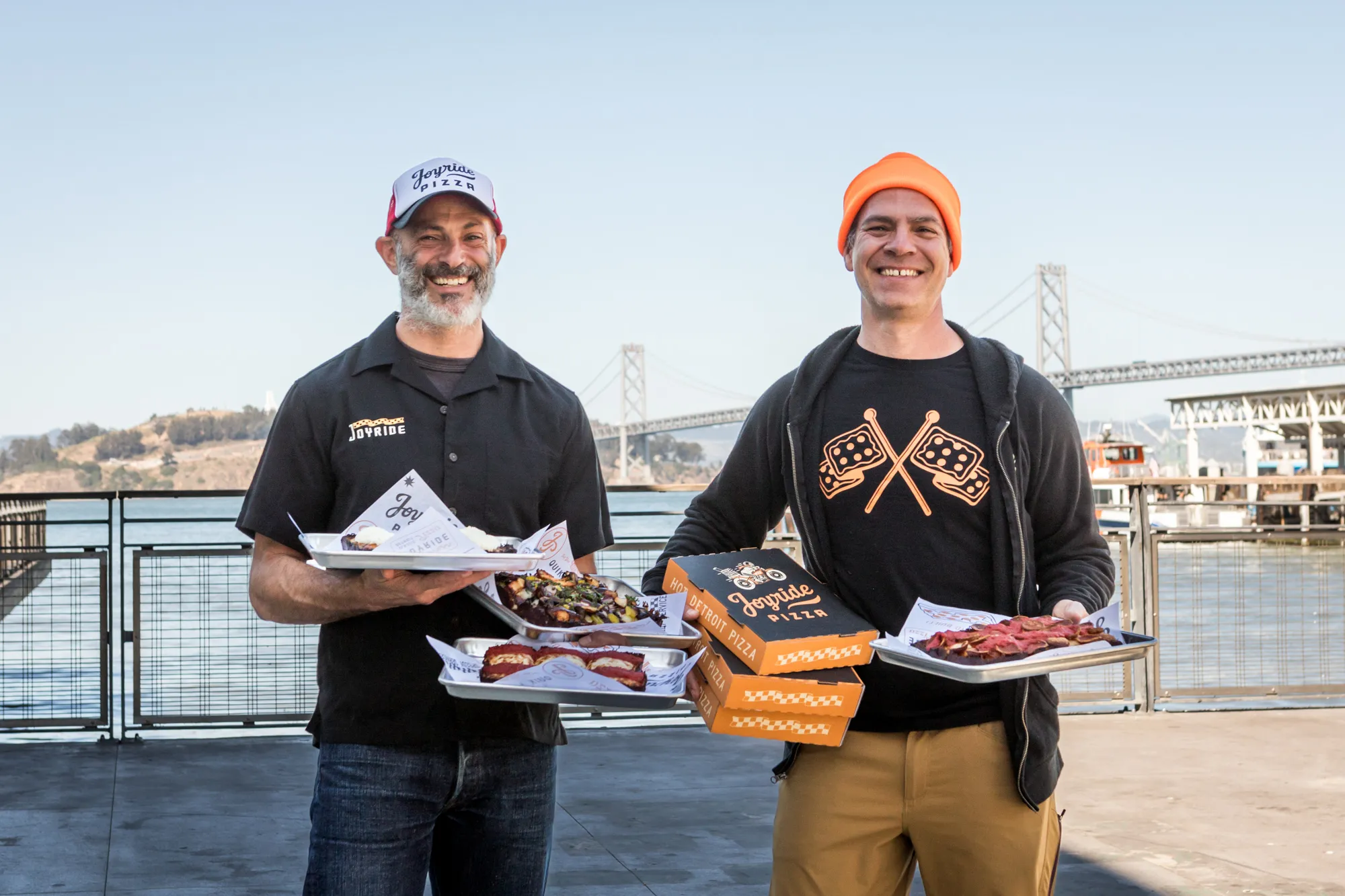 Joyride Pizza team holding pizzas on the Embarcadero waterfront with the Bay Bridge behind