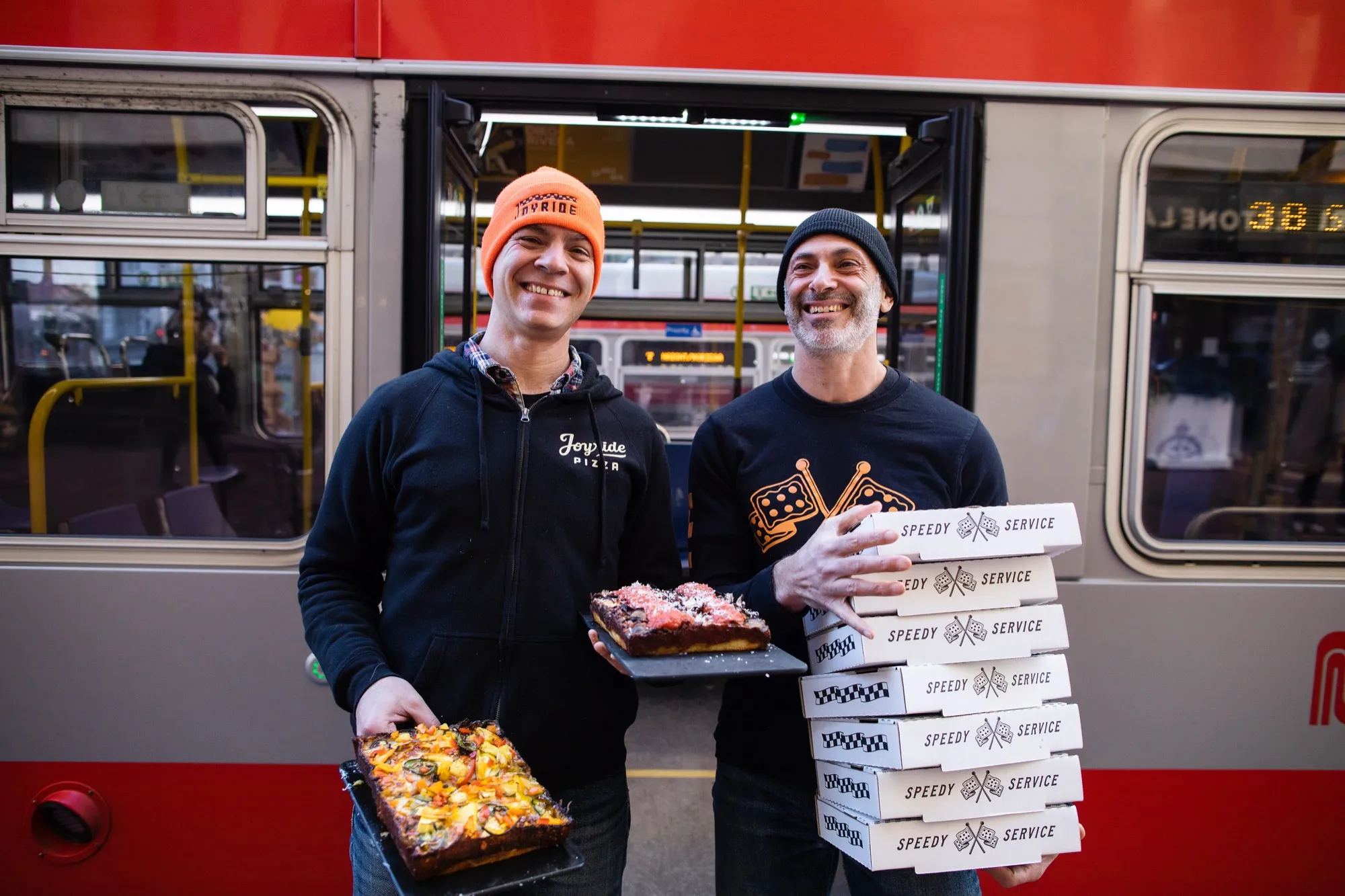 Joyride team holding pizzas and boxes beside a San Francisco streetcar downtown