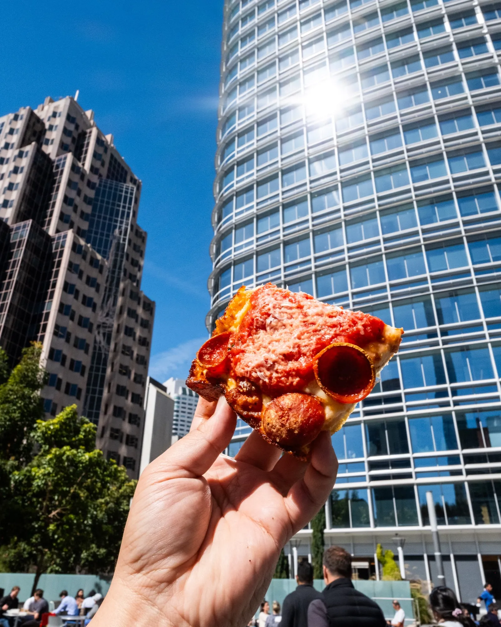A Detroit-style slice held up against the downtown high-rises at the rooftop beer garden